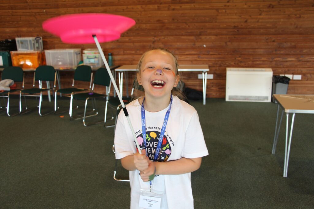 Young girl spinning a plate on a stick beaming at the camera